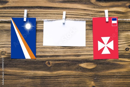 Hanging flags of Marshall Islands and Wallis And Futuna attached to rope with clothes pins with copy space on white note paper on wooden background.Diplomatic relations between countries. photo