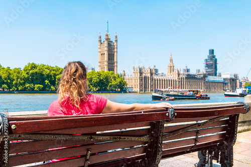 Photography Young woman sitting on bench in London looking at cityscape skyline of city with