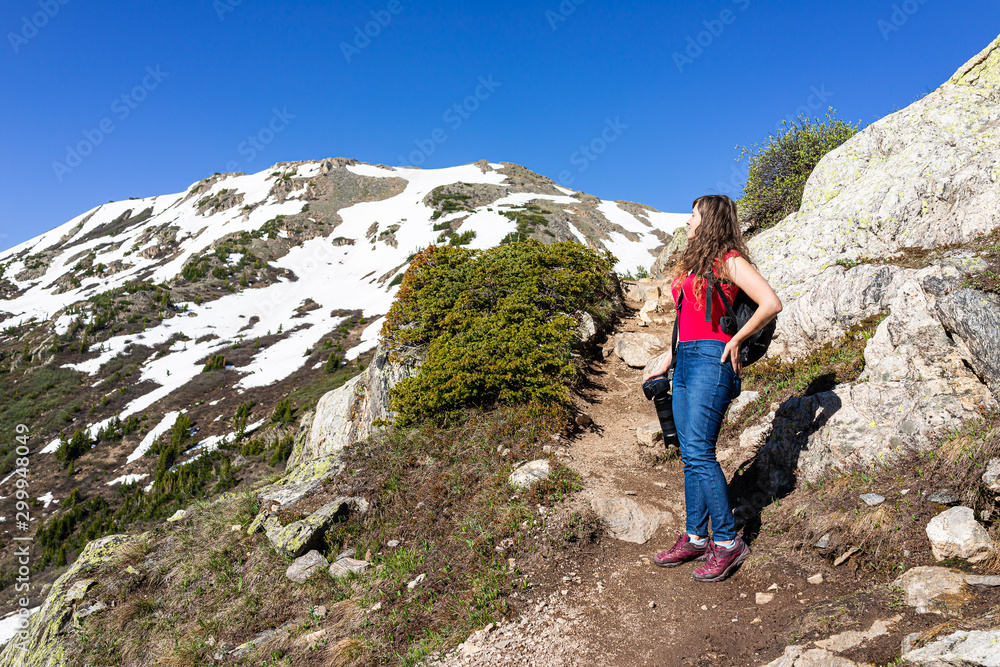 Woman photographer standing looking at view on Linkins Lake trail on Independence Pass in rocky mountains near Aspen, Colorado in early summer of 2019 with snow