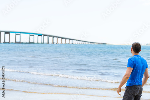 Young man back on beach bay shore looking at Pensacola bay bridge on US route highway road 98 in Navarre, Florida Panhandle near Gulf of Mexico © Andriy Blokhin