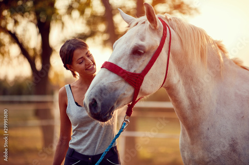 Smiling woman petting a horse on a ranch on a sunny summer day.