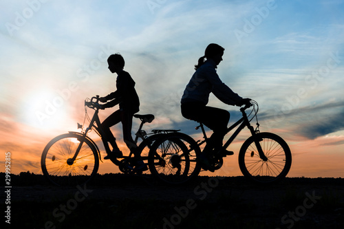 Boy and young girl riding bikes in different directions, silhouettes of riding persons at sunset in nature