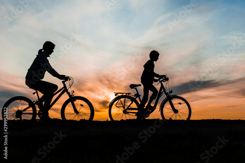 Boy and young girl riding bikes in countryside , silhouettes of riding persons at sunset in nature