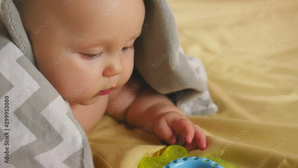 A chubby four months baby covered with a blanket lies on his tummy and