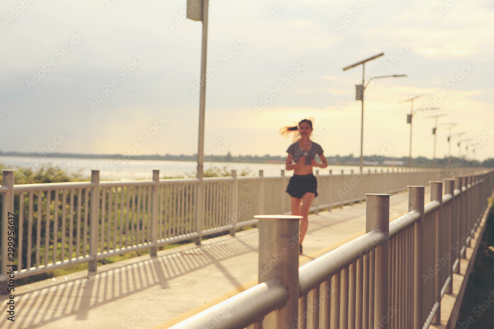 A good-looking woman is jogging in the evening. Focus on the bridge