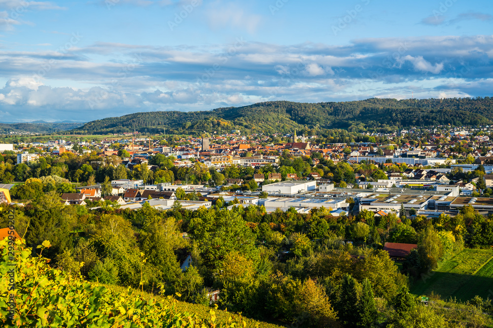 Obraz premium Germany, Wide aerial view above houses, church and roofs of schorndorf city in valley between forested hills in warm evening sunset light