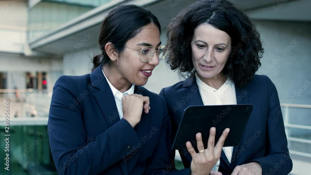Content businesswomen with digital devices. Focused multiethnic businesswomen in formal wear standing together on street and using digital tablet, slider shot. Technology concept Content businesswomen with digital devices. Focused multiethnic businesswomen in formal wear standing together on street and using digital tablet, slider shot. Technology concept