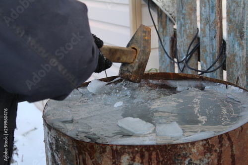  photo frozen water in a barrel.the tank is metal.the water was icy cold.a man breaks the ice on the surface of the water.works with a hammer.