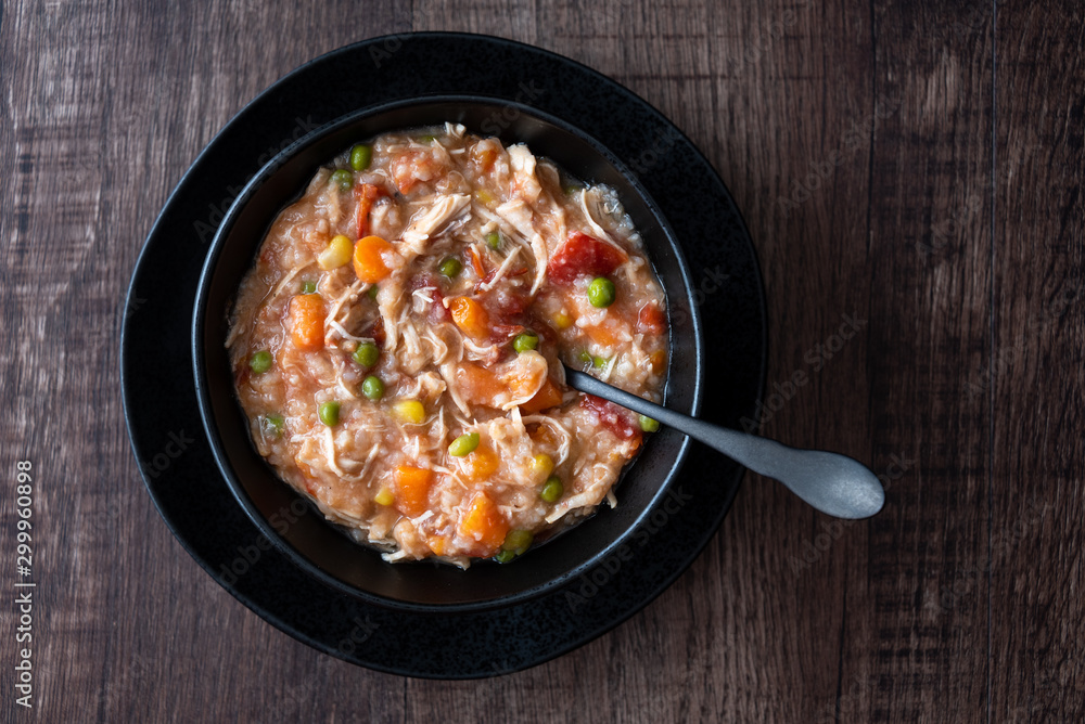 Puerto Rican Chicken Rice Soup in a black stoneware bowl and saucer on a dark wood table, black metal spoon Puerto Rican Chicken Rice Soup in a black stoneware bowl and saucer on a dark wood table, black metal spoon