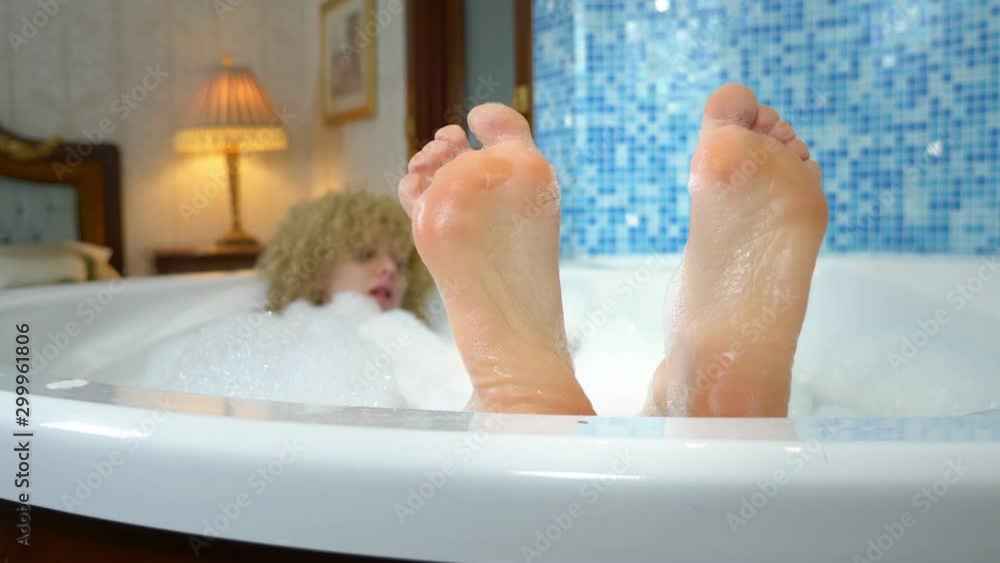 A beautiful smiling woman is lying in the bath with foam, her feet are visible from the water, the girl is dancing in feet. young naughty girl relaxes in the jacuzzi A beautiful smiling woman is lying in the bath with foam, her feet are visible from the water, the girl is dancing in feet. young naughty girl relaxes in the jacuzzi