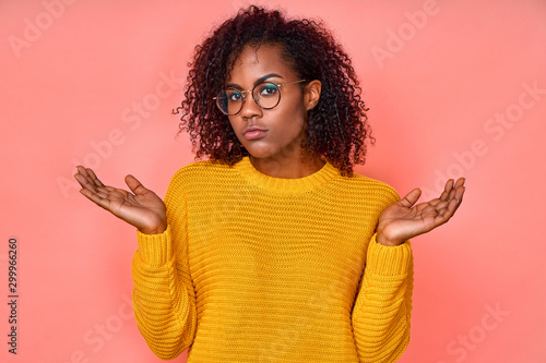 Tableau sur toile Isolated shot of confused beautiful woman with dark skin, curly haircut, spreads