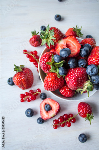 Fresh berries  strawberries  blueberries  red currant  in a white bowl on a white table  shallow depth of field
