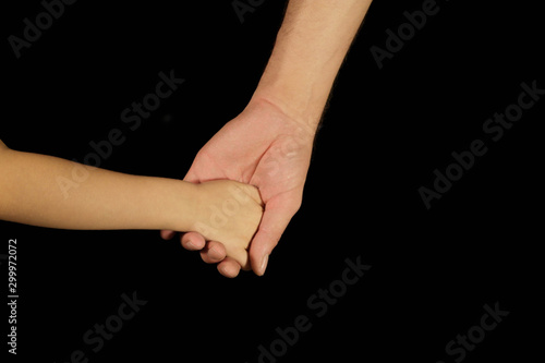Father holds son for hand. Isolated men and children palms on a black background. The concept of family relations, love, kindness and spiritual support. Hands close-up rear view and copy space.