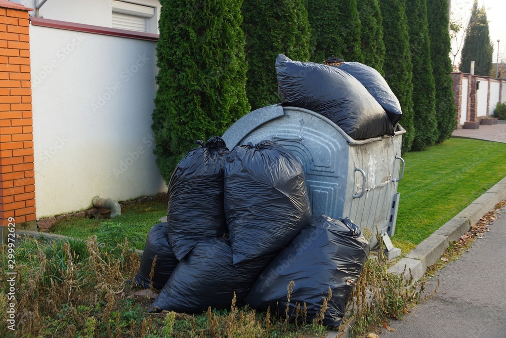 heap of black full garbage bags in a gray iron trash can on the street heap of black full garbage bags in a gray iron trash can on the street