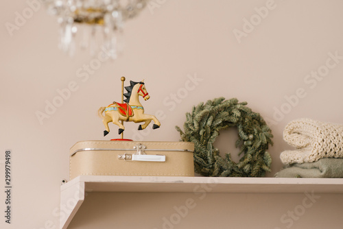 Wooden horse toy, a beige suitcase on a shelf and a Christmas wreath in the interior of a living room or dining room home photo