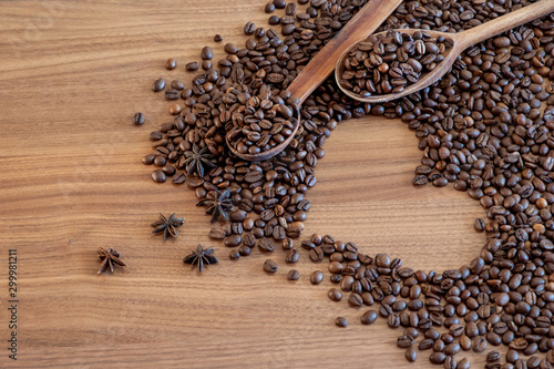 Coffee beans spilled on a heart-shaped wooden table with spices with two wooden spoons.