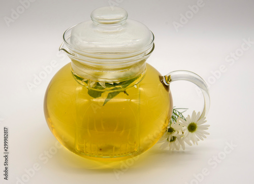 Transparent teapot with chamomile tea. A few of the flowers of the medicinal chamomile.