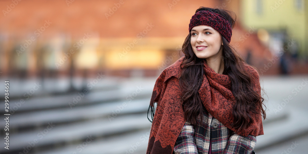 Beautiful joyful woman portrait in a city. Smiling  girl wearing warm clothes and hat  in winter or autumn. Christmas time with  unfocus lights on backgrounde. Copy space - obrazy, fototapety, plakaty 