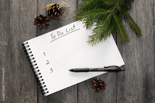 Planning new year. Notebook with to do list, Christmas tree branches and pinecones on wooden background top view