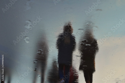 Dark shadows of people on wet pavement. Human silhouettes reflect on the wet road.
