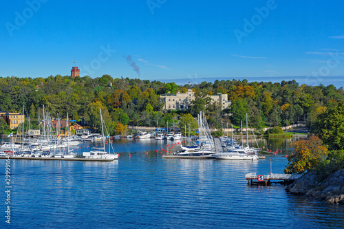 Boats and yachts docked at small marina along the waterfront of Djurgarden island at sunny autumn morning with reflections in the water. Stockholm, Sweden photo