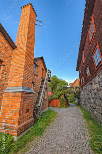 Narrow cobblestone street between well-preserved red brick building and traditional red wooden dwelling houses on stone hill. Stockholm, Sweden. photo