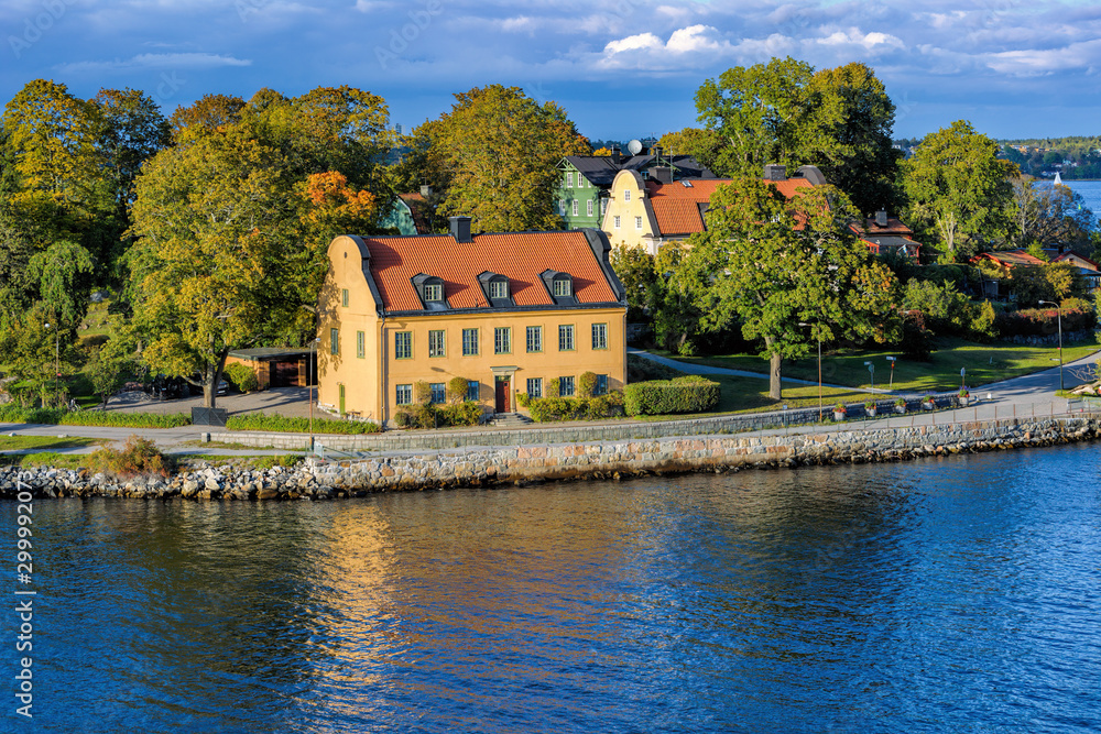 Φωτογραφία Yellow ancient house with red tiled roofs on waterfront of island Djurgarden at bright sunny day with autumn forest on the background