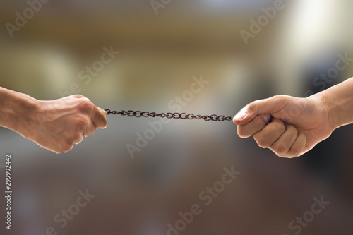 Close up shot of pair of hands playing tug of war with a rusted metal chain with blurred background of the corporate sector of the office parking area. photo