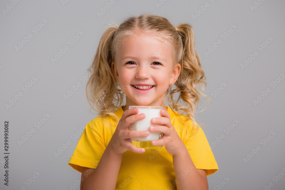 little blonde girl in yellow tank top holding a glass of milk on a light background, space for text little blonde girl in yellow tank top holding a glass of milk on a light background, space for text