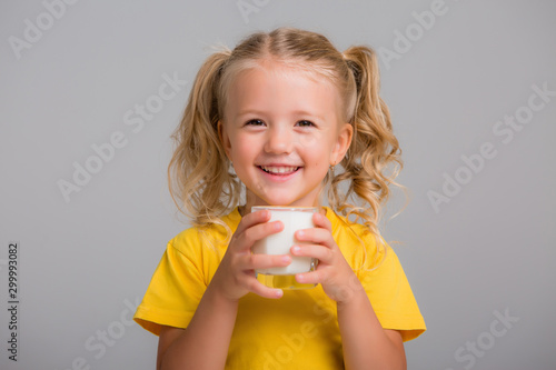 little blonde girl in yellow tank top holding a glass of milk on a light background, space for text