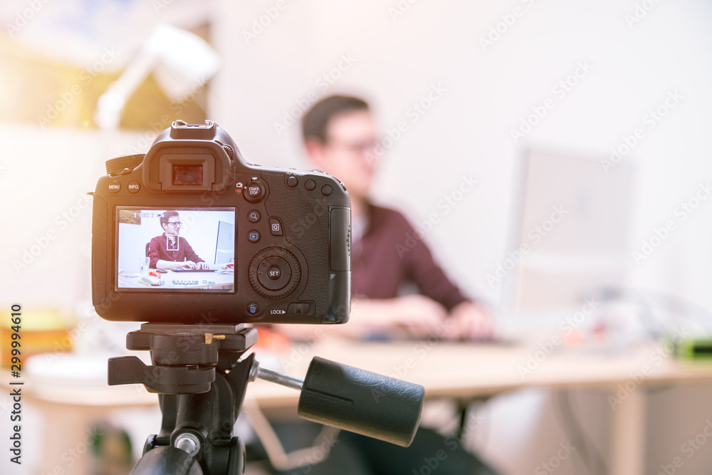 Video blogger at home: Camera on tripod is filming a young man sitting on his working place Video blogger at home: Camera on tripod is filming a young man sitting on his working place