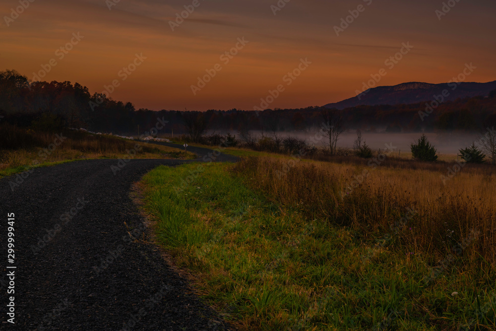 Amazing dreamy sunrise over Shawangunk Mountains, New York, featuring country road passing through farmland on the foreground and mountains on the background on foggy autumn morning