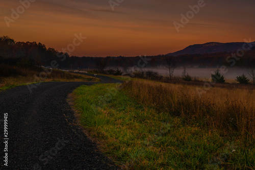 Amazing dreamy sunrise over Shawangunk Mountains  New York  featuring country road passing through farmland on the foreground and mountains on the background on foggy autumn morning