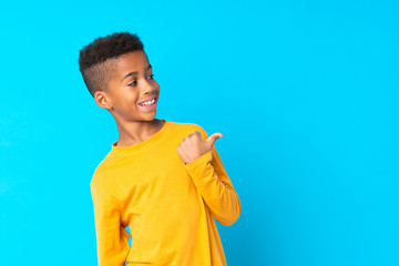 African American boy over isolated blue background pointing to the side to present a product