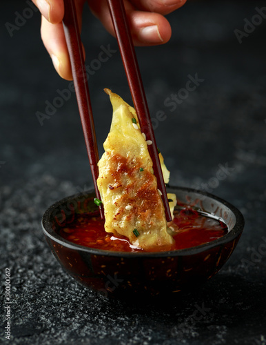 Chopsticks holding and dipping meat dumplings, fried yaki gyoza in sweet chilli sauce.