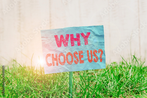 Text sign showing Why Choose Us Question. Business photo showcasing list of advantages and disadvantages to select product service Plain empty paper attached to a stick and placed in the green grassy