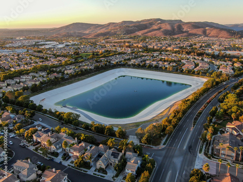 Aerial view of water recycling reservoir surrounded by suburban neighborhood with big villas during sunset time, South California