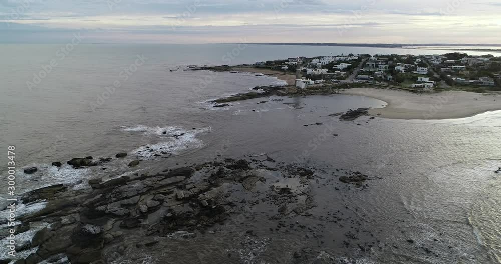 Aerial drone scene of panoramic landscape of rocky peninsula with lighthouse and touristic village at background. Descending above water and rocks. Jose Ignacio town, Maldonado, Uruguay Aerial drone scene of panoramic landscape of rocky peninsula with lighthouse and touristic village at background. Descending above water and rocks. Jose Ignacio town, Maldonado, Uruguay