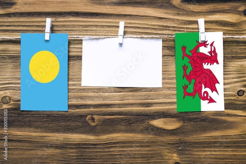 Hanging flags of Palau and Wales attached to rope with clothes pins with copy space on white note paper on wooden background.Diplomatic relations between countries. photo