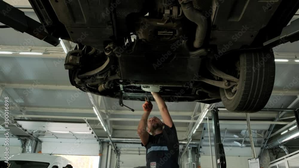 Auto mechanic working underneath car lifting machine at the garage. Auto repair shop, Car service, repair. Auto mechanic working underneath car lifting machine at the garage. Auto repair shop, Car service, repair.