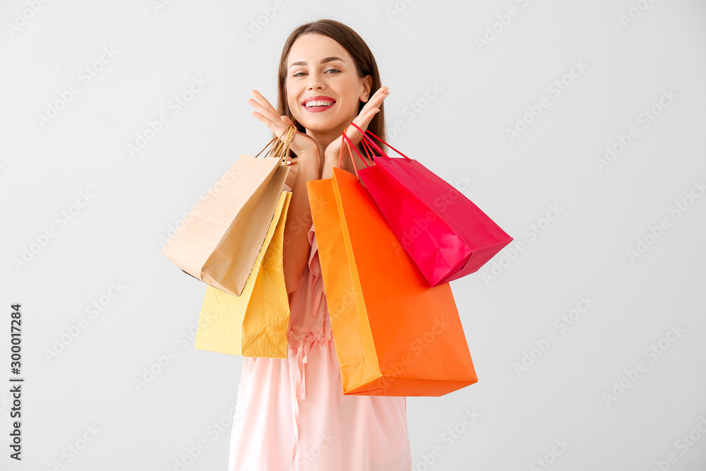 Beautiful young woman with shopping bags on light background