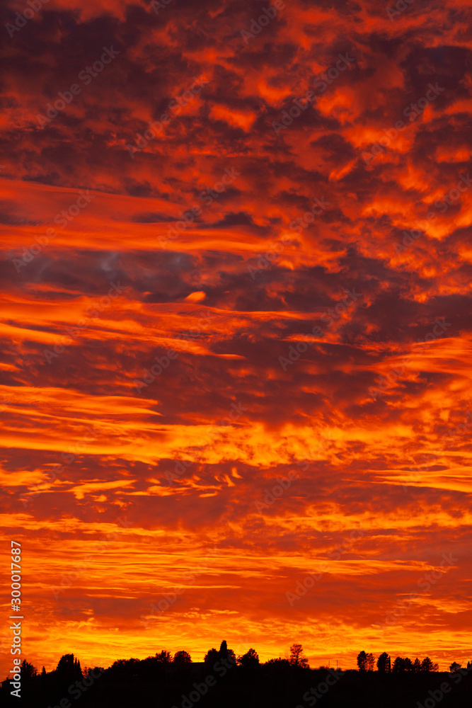 Beautiful sunset in Tuscany, Italy. Dramatic sky, bright red and orange colors, dark silhouettes of hills and trees Beautiful sunset in Tuscany, Italy. Dramatic sky, bright red and orange colors, dark silhouettes of hills and trees