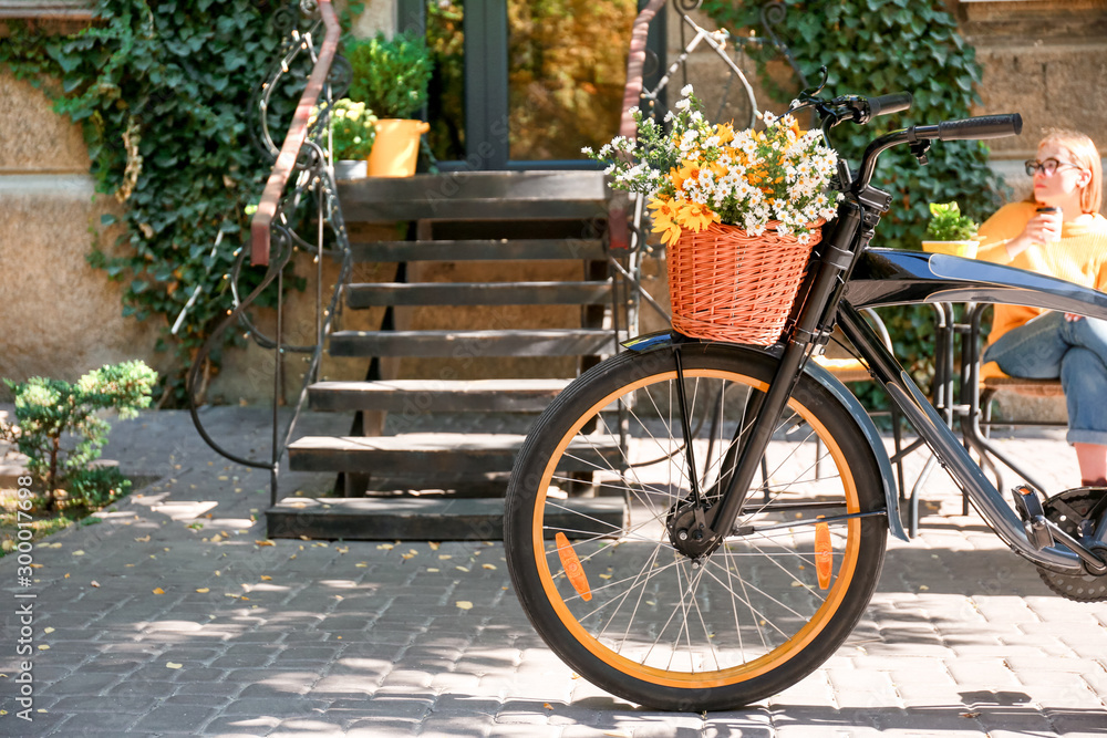 Modern bicycle with basket and bouquet of flowers on city street
