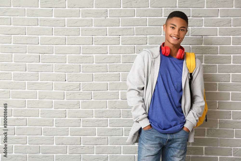 Portrait of African-American teenage schoolboy on brick background - obrazy, fototapety, plakaty 