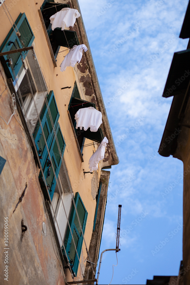 Italy, Liguria region, Cinque Terra. Small street in old town, view from botton to the top. Blue sky, yellow walls and green shutters, white clothes drying on the ropes Italy, Liguria region, Cinque Terra. Small street in old town, view from botton to the top. Blue sky, yellow walls and green shutters, white clothes drying on the ropes