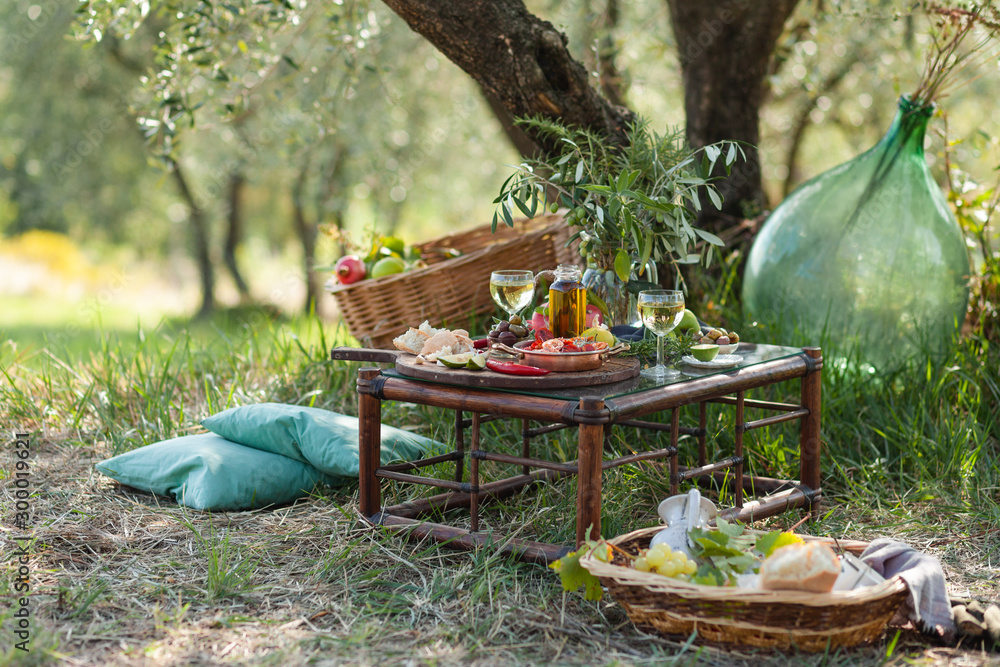 Romantic picnic under olive tree. Delicious italian meal served on a wooden  table. Baskets with food, branches in glass jar. Sunny autumn day. Italy,  Tuscany Stock Photo | Adobe Stock