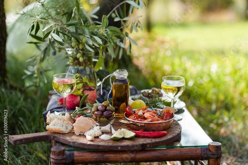 Romantic italian lunch outside for a couple: copper pan with delicious and spicy fried shrimps with herbs and garlic, wine, bread, olives. Bottle of olive oil. Luxury lifestyle, gourmet food