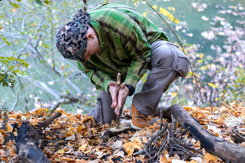 Man starting a fire in the wild using technique of friction with two sticks. Practicing survival craft and skills with primitive tools.