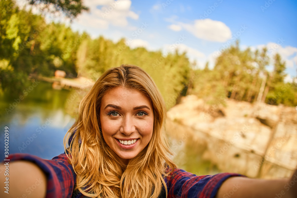 Female tourist exploring new places making a selfie photo. Portrait of handsome woman on nature near the lake at forest background. Female tourist exploring new places making a selfie photo. Portrait of handsome woman on nature near the lake at forest background.