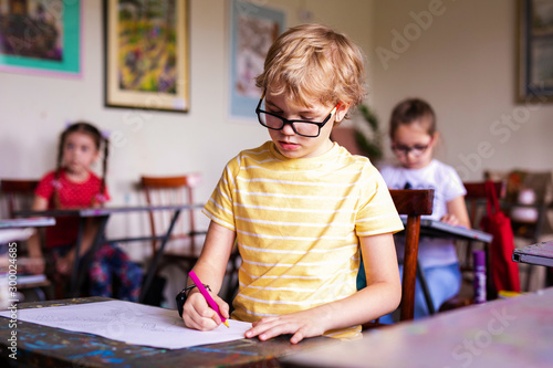 Blonde boy with glasses drawing. Group of elementary school pupils in classroom on art class. Russia, Krasnodar, May, 23, 2019